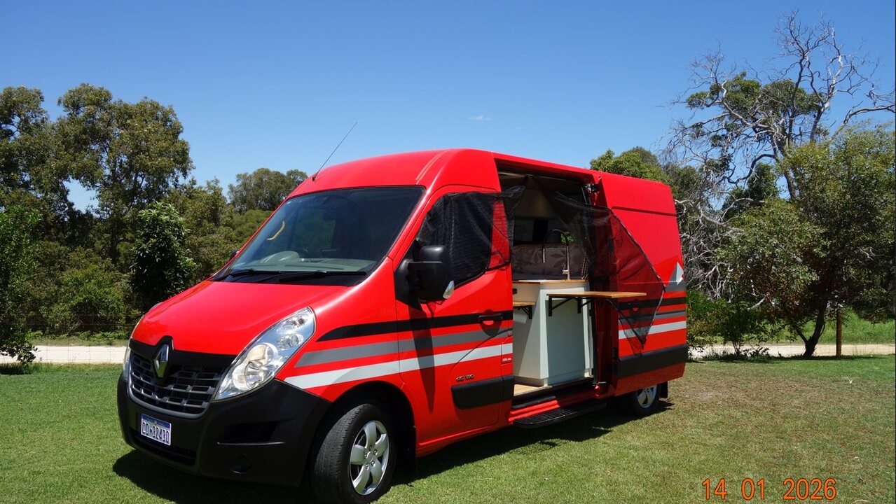 The finished red Renault Master campervan parked on grass with its side door open